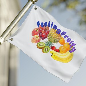 May include: A white flag with the words "Feeling Fruity" in purple script, and a watercolor illustration of various fruits. The fruits include apples, grapes, a pineapple, kiwi, strawberries, oranges, and bananas. The flag is attached to a silver pole.