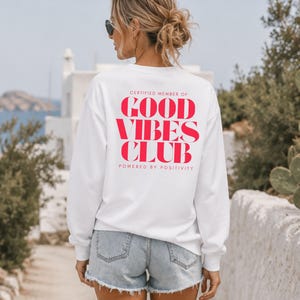 Könnte beinhalten: Weißes Sweatshirt mit dem roten Text "CERTIFIED MEMBER OF GOOD VIBES CLUB POWERED BY POSITIVITY". Das Sweatshirt wird mit Jeansshorts kombiniert. Das Bild wurde an einem sonnigen Tag im Freien aufgenommen.