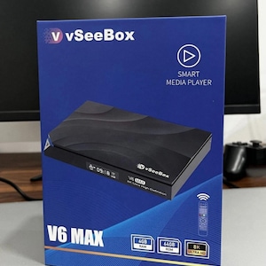 May include: A blue box with the text "vSeeBox" and "V6 MAX" on the front. The box contains a black smart media player. The box also displays the specifications: 4GB RAM, 64GB ROM, and 8K Ultra HD.
