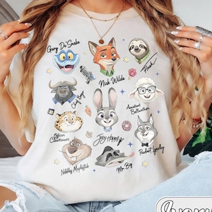 May include: Ivory-coloured t-shirt with cartoon illustrations of characters from a movie. The shirt features characters such as Nick Wilde, Judy Hopps, and Flash, with their names printed above. The word "Ivory" is printed at the bottom.