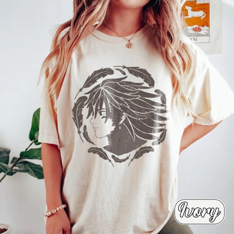 Pu&ograve; includere: Una t-shirt a maniche corte color avorio con una grafica circolare grigio scuro sul petto. Il design raffigura il profilo di un personaggio in stile anime con capelli lunghi e fluenti, circondato da un anello di piume sparse in cerchio.