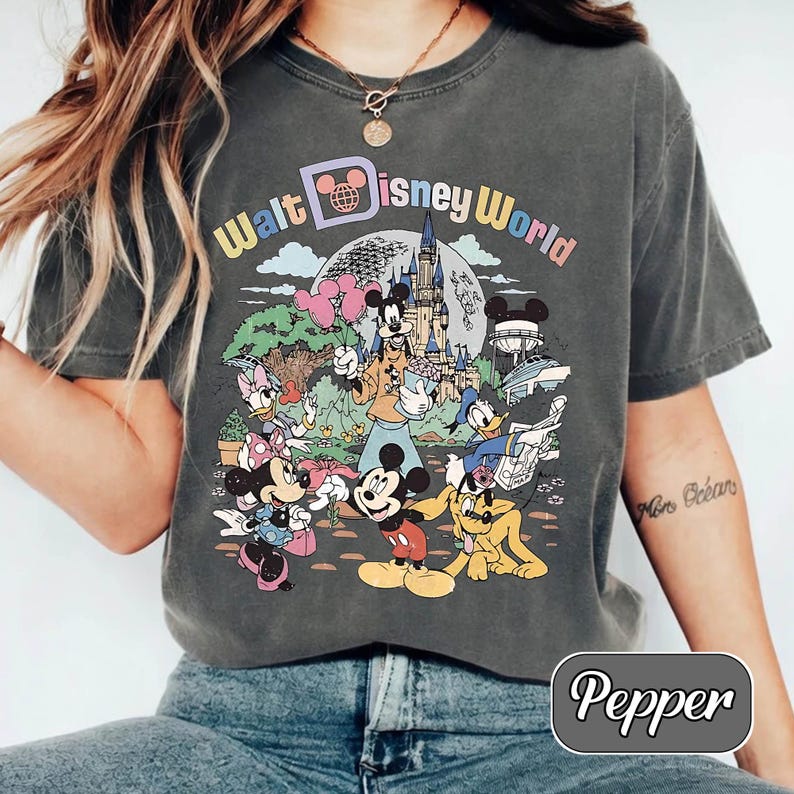 May include: A dark gray t-shirt featuring a colorful graphic of Disney characters and the text "Walt Disney World." The design includes Mickey Mouse, Minnie Mouse, Donald Duck, and other characters in front of a castle and other park attractions.