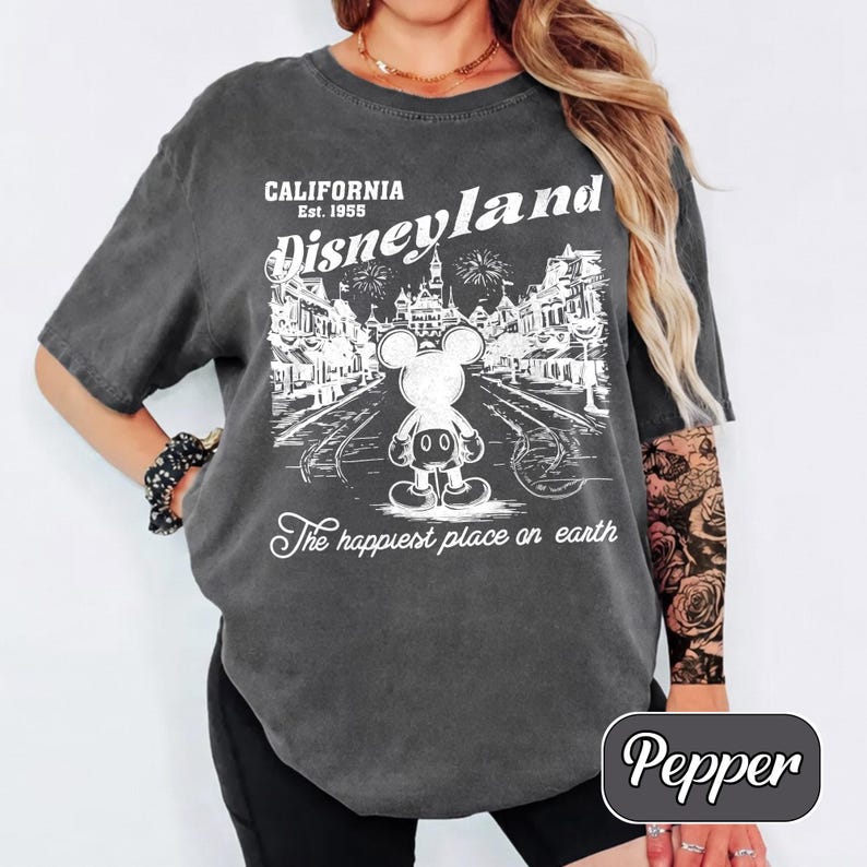 May include: Dark gray t-shirt with a white Disneyland graphic. The graphic includes the text "California Est. 1955 Disneyland" and a Mickey Mouse illustration. The phrase "The happiest place on earth" is also printed on the shirt.