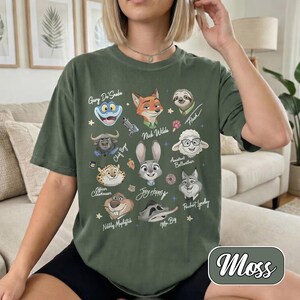 May include: A moss green t-shirt with cartoon character illustrations and names, including Nick Wilde, Judy Hopps, and Flash. The word "Moss" is in a green oval at the bottom right.