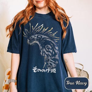 May include: A true navy blue short-sleeved t-shirt featuring a large, distressed graphic of a creature with tribal-style patterns and a spiky crest. Below the creature, the Japanese text "もののけ姫" is printed in a weathered white font.