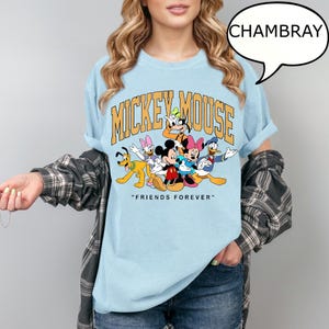 May include: Light blue t-shirt featuring a graphic of Mickey Mouse and friends. The design includes the text "MICKEY MOUSE" in gold lettering and the phrase "FRIENDS FOREVER" below the characters. The shirt is made of a soft material.