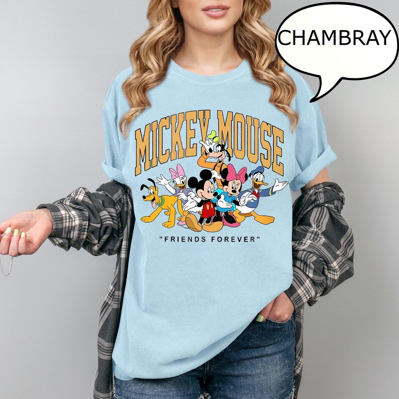May include: Light blue t-shirt featuring a graphic of Mickey Mouse and friends. The design includes the text "MICKEY MOUSE" in gold lettering and the phrase "FRIENDS FOREVER" below the characters. The shirt is made of a soft material.