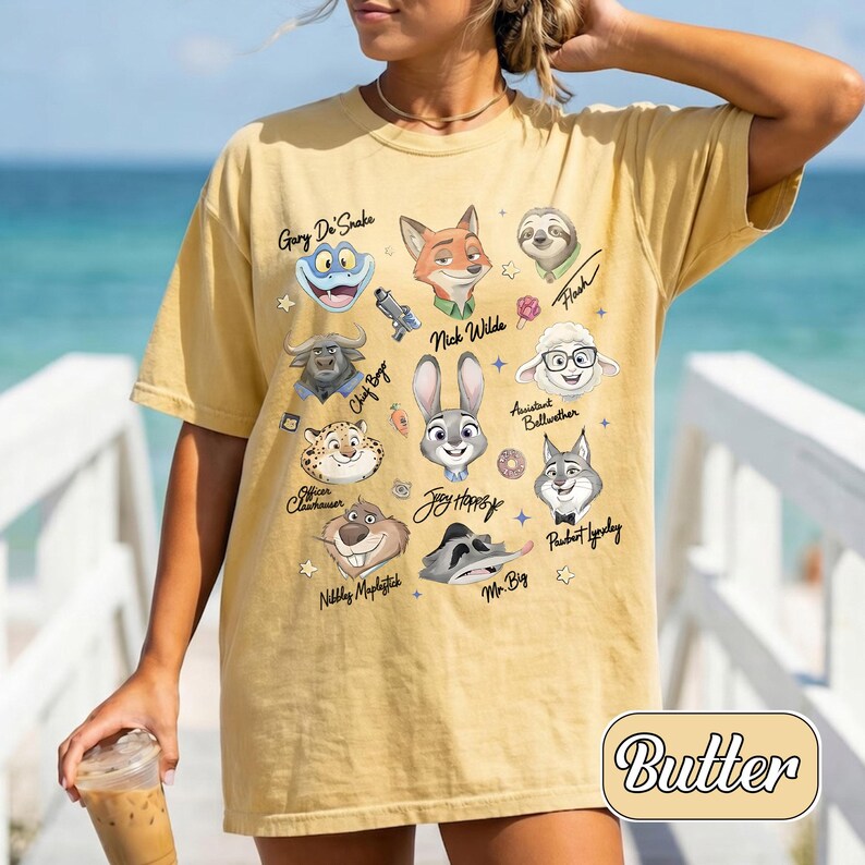 May include: A yellow t-shirt with cartoon characters from a movie. The shirt has the word "Butter" in a decorative font. The characters include a frog, fox, sloth, and others. The shirt is a casual style.