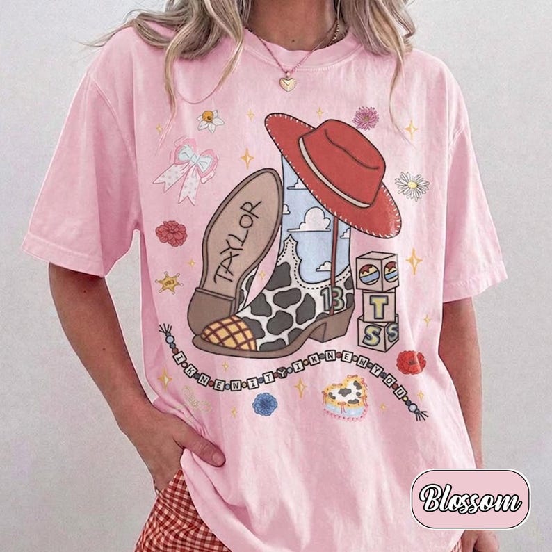Pu&ograve; includere: Una t-shirt rosa chiaro con una stampa grafica di uno stivale da cowboy con macchie di mucca e il nome TAYLOR, un cappello da cowboy rosso, blocchi con le lettere T, S e il numero 13, un fiocco, fiori e una catena di perline con testo.