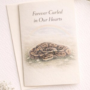 May include: A folded card with the text "Forever Curled in Our Hearts" above a watercolor illustration of a coiled snake on a bed of grass and flowers. The card is accompanied by a blank envelope.