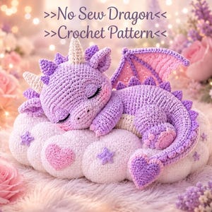 May include: A purple crocheted dragon with a cream-coloured horn and wings, sleeping on a white crocheted cloud decorated with pink hearts and purple stars. The text >>No Sew Dragon<< >>Crochet Pattern<< is displayed above the dragon.