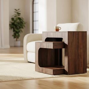 May include: A two-tiered, wooden side table with a dark brown finish. The table has a unique, open design with rounded corners. A small mug sits on the top tier. The table is placed on a light-colored rug in a living room setting.