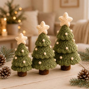 Pode incluir: Três árvores de Natal de crochê de alturas variadas, cada uma com um corpo em camadas verde-escuro com pequenos detalhes de bolinhas brancas e uma estrela creme no topo. As árvores têm bases cilíndricas castanhas sobre uma superfície de madeira.