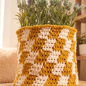 May include: A handmade crochet basket in a yellow and white geometric pattern, filled with faux lavender plants. The basket has a cylindrical shape and a thick, textured appearance, perfect for home decor.