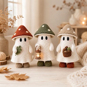 May include: Three crocheted ghost figures with mushroom caps in red, green, and beige. The ghosts have white bodies, black oval eyes, and pink cheeks. One holds a green leaf, one carries a small lit lantern, and one holds a basket of acorns.