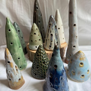 May include: A collection of eleven cone-shaped ceramic sculptures in various sizes and colors, including shades of green, blue, brown, and white. Each piece features multiple small circular cutouts across its surface, with some having textured finishes and others smooth, glossy glazes.