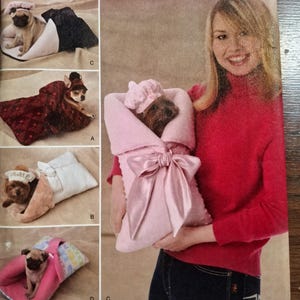 May include: A Simplicity sewing pattern envelope 2744 for pet accessories. The front displays four images of small dogs wearing hats and wrapped in fabric pouches with bows. The text includes Simplicity, 2744, and Designs for Dinky Dogs.