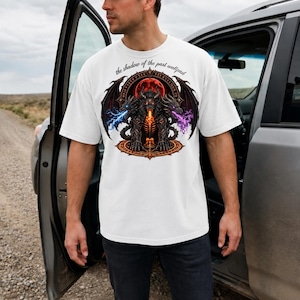Puede incluir: Camiseta blanca con un diseño detallado de una criatura de fantasía con alas, rodeada de rayos y llamas. El texto "the shadow of the past wallpad" está encima del gráfico. La persona lleva la camiseta junto a un coche.