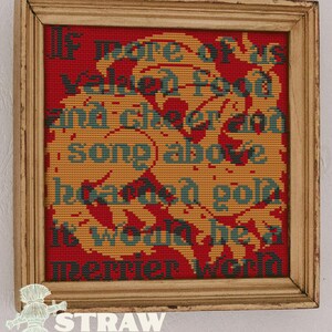 May include: A framed cross-stitch sampler featuring a red background with a large yellow dragon motif. The text reads: If more of us valued food and cheer and song above hoarded gold, it would be a merrier world. The frame is light-colored wood.