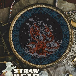 May include: A round, framed cross-stitch featuring a ship being attacked by a giant orange kraken. The design is set against a dark blue and black background with a rope-wrapped frame. The text "STRAW BEAR" is visible at the bottom.