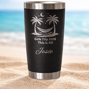 Puede incluir: Vaso térmico negro con borde y base plateados. Presenta una escena de playa con palmeras, una hamaca y el texto "Girls Trip 2026 This is 50!" y el nombre "Josée" en cursiva.