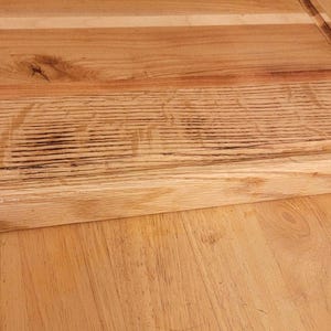 Op de afbeelding: Een rechthoekige houten snijplank met een groef voor sap. De plank is gemaakt van lichtgekleurd hout met zichtbare nerf en een donkerder houten accent aan de zijkant. De plank ligt op een houten oppervlak.