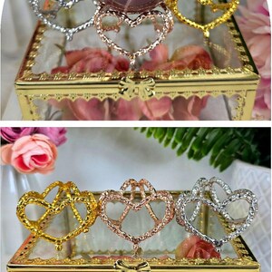 May include: A decorative sphere stand with heart-shaped holders in gold, silver, and rose gold. A clear glass box with a gold frame holds the stands, and a pink sphere rests on one. The text "Sphere Stand - HEARTS" is at the bottom.