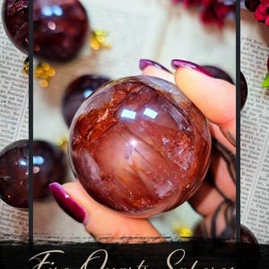 Peut inclure: Gros plan sur une sphère de quartz de feu, également appelée quartz hématite, tenue dans une main. La sphère est de couleur brun-rouge translucide avec des stries internes. Le texte "Fire Quartz Spheres" est affiché en dessous.