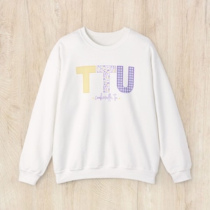 May include: White sweatshirt with the letters "TTU" in yellow, floral, and purple gingham patterns. Below the letters is the text "- cookeville, tn -" in a green script. The sweatshirt has a crew neck and long sleeves.