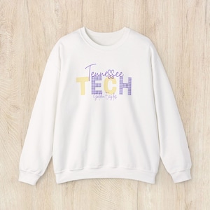 May include: White crewneck sweatshirt with the words "Tennessee TECH Golden Eagles" in purple and yellow. The word "TECH" is in a yellow block letter style, and the "H" is a purple gingham pattern.