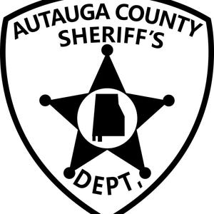 May include: A black and white shield-shaped emblem. The text "AUTAUGA COUNTY SHERIFF'S DEPT." is displayed around a black star with a white circle in the center, containing a black outline of the state of Alabama.