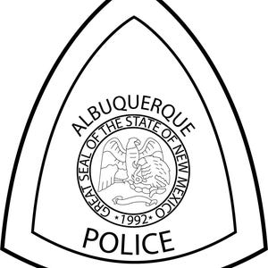 May include: Black and white Albuquerque Police badge. The badge is shield-shaped with a double outline. The words "ALBUQUERQUE" and "POLICE" are displayed. The center features a circular emblem with an eagle and the words "GREAT SEAL OF THE STATE OF NEW MEXICO *1992*."