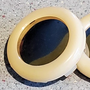 Puede incluir: Dos compactos redondos de color crema con ribetes dorados y espejos negros.