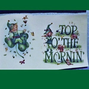May include: A green shamrock with a small leprechaun sitting on it. The leprechaun is wearing a green hat and a green suit. The text "Top o' the mornin'" is written in green letters on a white background.