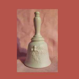 May include: A white ceramic bell with a holly leaf design. The bell has a rounded top and a wide base.