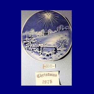Puede incluir: Un plato de Navidad azul y blanco con una escena de invierno de una iglesia, árboles y una valla. El plato tiene una estrella en el cielo y el texto "Christmas 1976".