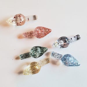 Może przedstawiać: Sześć kolorowych szklanych ozdób z brokatem i przezroczystym trzonkiem. Ozdoby mają kształt łzy, w kolorach takich jak różowy, zielony, niebieski i złoty. Niektóre mają symbole kart do gry.