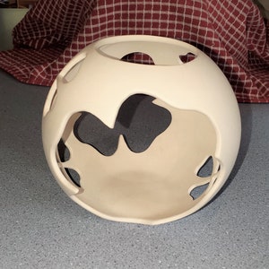 May include: A white ceramic sphere with cut-out designs. The sphere is hollow and has a smooth, matte finish.