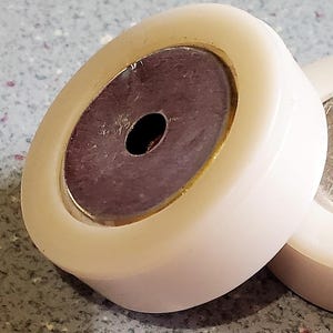 May include: Close-up of a white plastic roller with a gold rim and a dark brown center. The roller has a small hole in the center.