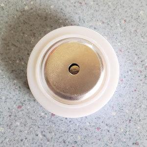 May include: A white plastic bottle stopper with a silver metal cap and a small hole in the center.