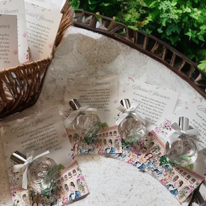 Puede incluir: Recuerdos de despedida de soltera, que incluyen peque&ntilde;os frascos de perfume con tapas plateadas y lazos de cinta blanca, presentados en tarjetas decorativas con ilustraciones florales y arquitect&oacute;nicas. Una cesta de mimbre y vegetaci&oacute;n en el fondo.