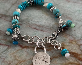May include: A turquoise and silver bracelet with a charm that says "Good Vibes". The bracelet has a variety of turquoise beads, silver beads, and a silver chain.