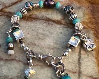 May include: A silver charm bracelet with turquoise and silver beads, a black pearl, and several silver charms. The bracelet has a lobster claw clasp.