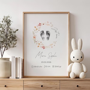 Könnte beinhalten: Ein gerahmter Druck mit Babyfüßen in einem floralen Kranz. Der Druck zeigt den Namen "Marie Sophie", das Datum 20.02.2026, die Uhrzeit 08:43 Uhr, die Länge 52 cm und das Gewicht 3240 gr. Ein dekorativer Hase befindet sich auf einer Holzoberfläche.
