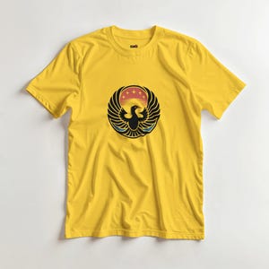 Peut inclure: Un t-shirt jaune avec un motif circulaire d'un oiseau stylisé aux ailes déployées. Le motif comprend une silhouette d'oiseau noir, un coucher de soleil rouge et orange et un contour bleu. Le t-shirt est en matière souple.