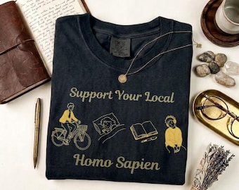Camiseta "Apoya a tu Homo Sapien local", camiseta divertida con temática humana, camiseta con humor científico, colores cómodos.
