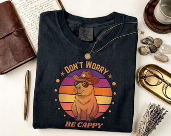 Camiseta "Don't Worry Be Cappy", divertida camiseta con meme de capibara, colores cómodos, estampado retro de puesta de sol.
