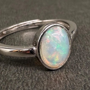Pode incluir: Um anel de prata com uma pedra de opala oval. A opala exibe cores iridescentes de verde, azul e rosa. O anel tem um design simples e elegante, perfeito para uso diário.