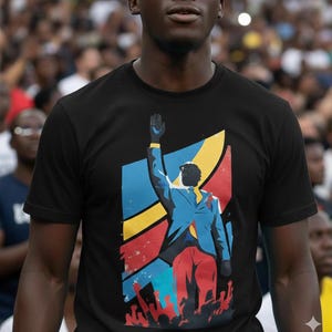 Puede incluir: Camiseta negra con un diseño gráfico de una persona con traje azul levantando la mano, sobre un fondo de la bandera de la República Democrática del Congo. El diseño incluye elementos rojos, amarillos y azules.