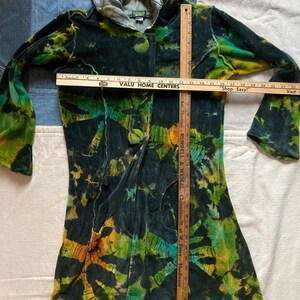 K&ouml;nnte beinhalten: Eine lange Kapuzenjacke mit Batikmuster in Gr&uuml;n-, Gelb- und Schwarzt&ouml;nen. Die Jacke hat einen Knopfverschluss und lange &Auml;rmel. Ein Holzlineal liegt auf der Jacke und misst ca. 76 cm. Der Text "VALU HOME CENTERS" ist sichtbar.